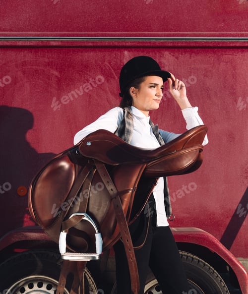 Preview: Serious young woman sitting outdoors and holding seddle