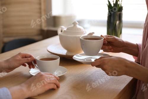 Preview: Women with cups of tea at table near window indoors, closeup