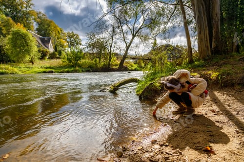 Preview: Young girl playing by river with water during nature exploration activity in countryside setting