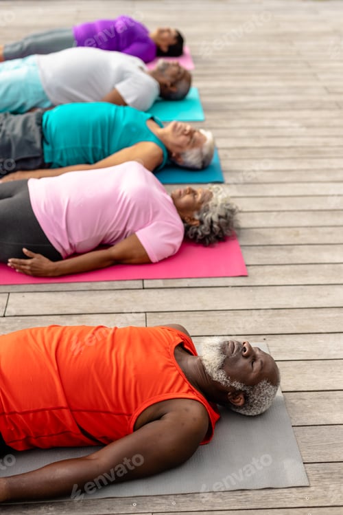 Preview: Multiracial senior friends with eyes closed exercising while lying on mats over hardwood floor