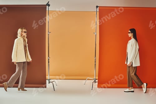 Preview: interracial models in outerwear and sunglasses walking near colorful backdrop, fall fashion concept