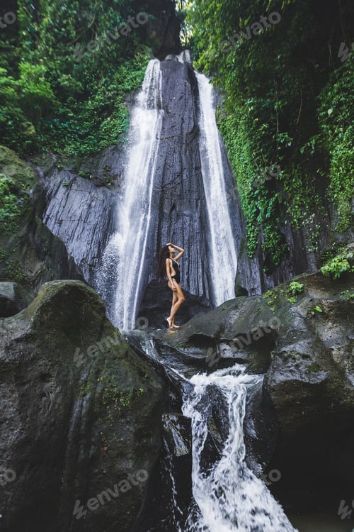 Preview: Woman enjoying near hidden in jungle cascade waterfall in Bali. Slim body and black swimsuit