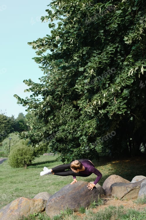 Preview: Flexible fit young woman practicing yoga asana, balance horizontal handstand on stone in park