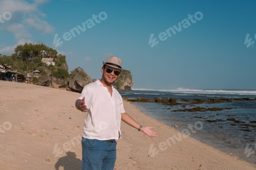 Preview: Smiling young Asian man doing invite hand gesture while standing by the Drini beach, Yogyakarta.