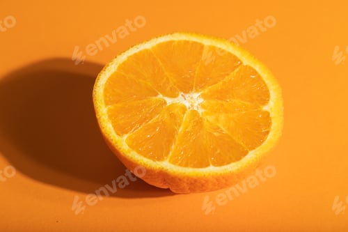Preview: Ripe cut orange on orange pastel background. Side view, close up, hard light.