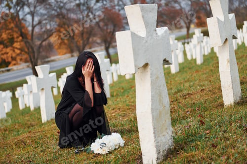 Preview: Young woman in black clothes visiting cemetery with many white crosses