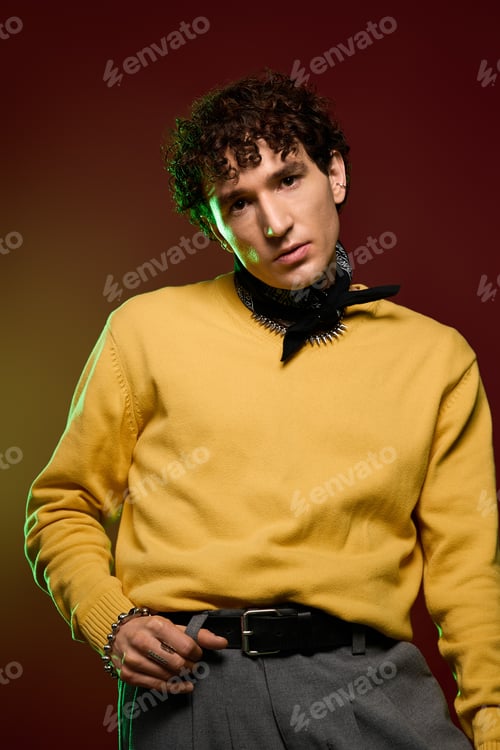 Preview: Stunning man in vibrant yellow sweater poses with stylish confidence against a rich backdrop