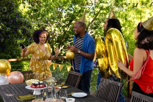 Visualização: Amigos comemorando aniversário ao ar livre com bolo e balões, usando chapéus de festa