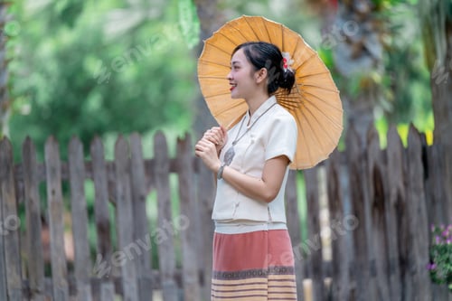 Preview: Thai woman wearing traditional Lanna dress holding paper umbrella in garden