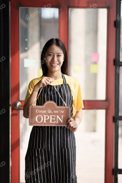 Preview: Small business owner smiling while turning the sign for the opening of the shop. Close up of woman
