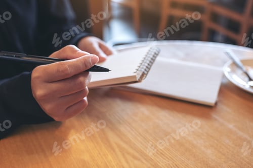 Preview: Closeup image of a woman holding and writing on blank notebook on table in cafe