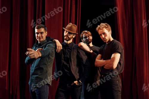 Preview: Standing against red curtains. Group of actors in dark colored clothes on rehearsal in the theater