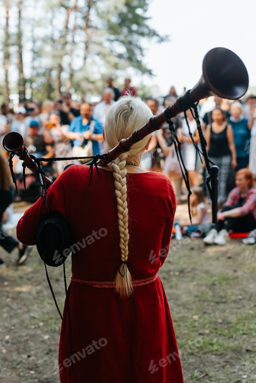 Preview: Folk concert outdoors. Back view of a woman musician in a medieval costume playing the bagpipes