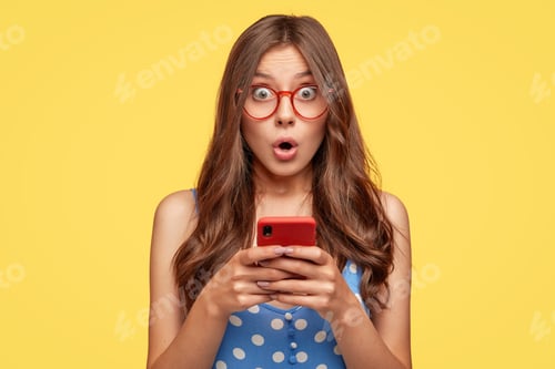 Preview: Surprised Woman Holding Phone Against Yellow Background