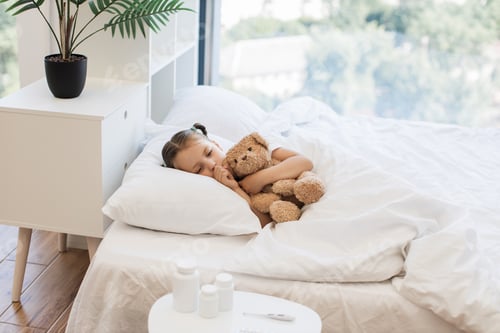 Preview: Fatigued cute girl hugging toy bear and coughing in bed