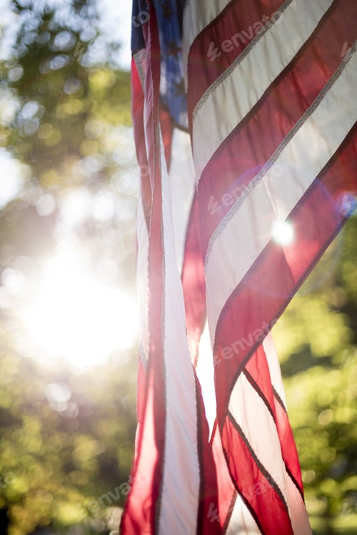 Preview: Vertical closeup shot of the united states flag with the sun shining in the background