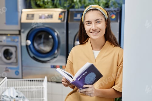 Preview: Young smiling woman with open book in purple cover looking at camera