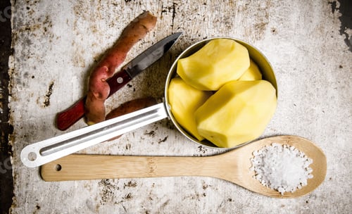 Preview: The peeled potatoes in a metal saucepan with a spoonful of salt on the rustic background .