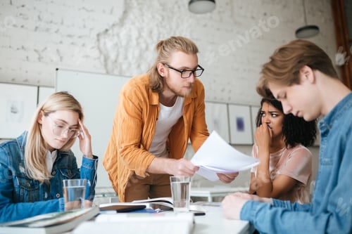 Preview: Group of upset students sitting at the table with books listening teacher