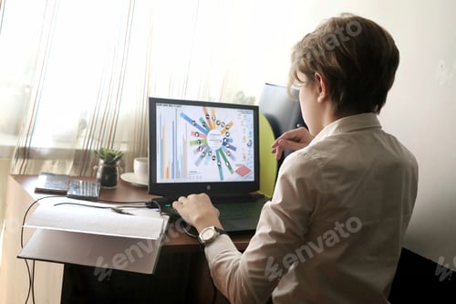 Preview: A young aspiring businessman sits in front of his notebook at his desk and studies the stock market