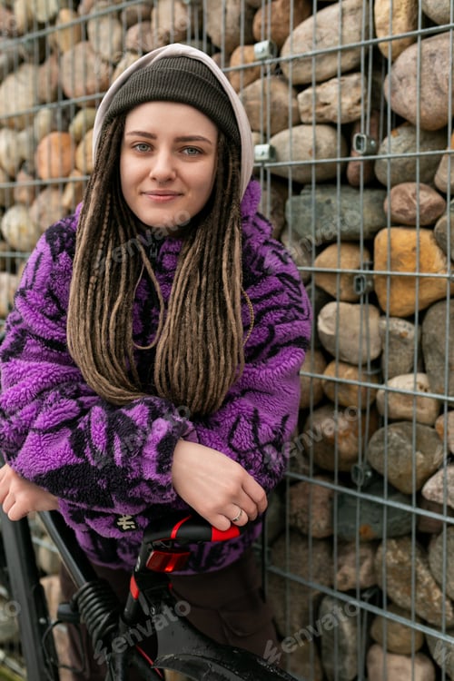 Preview: Lifestyle concept. Young woman with piercings and dreadlocks rides a bicycle