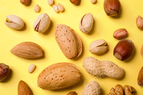Preview: Different delicious nuts on yellow background, flat lay