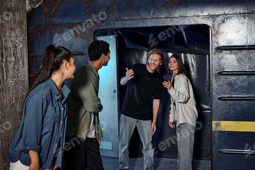 Preview: cheerful young man gesturing and inviting friends to subway wagon inside of escape room, quest