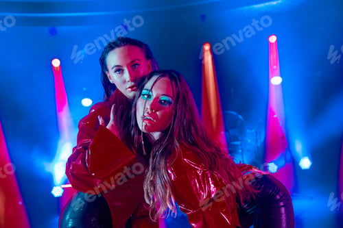 Preview: Close-up shot of two attractive women posing on a club stage with neon lights in the background