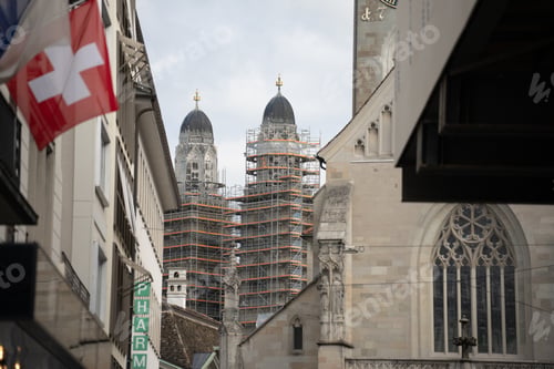 Preview: Grossmunster twin towers covered in scaffolding, with a swiss flag flying nearby in zurich