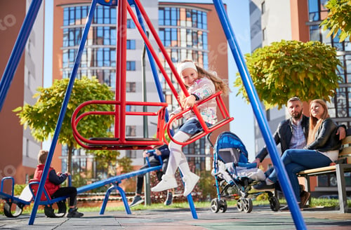 Preview: Little girl swinging with parents behind.