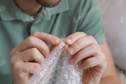 Preview: Man popping bubble wrap indoors, closeup view. Stress relief