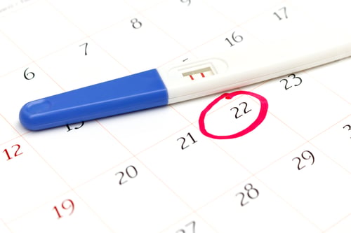 Preview: Pregnancy test with positive result lying on calendar