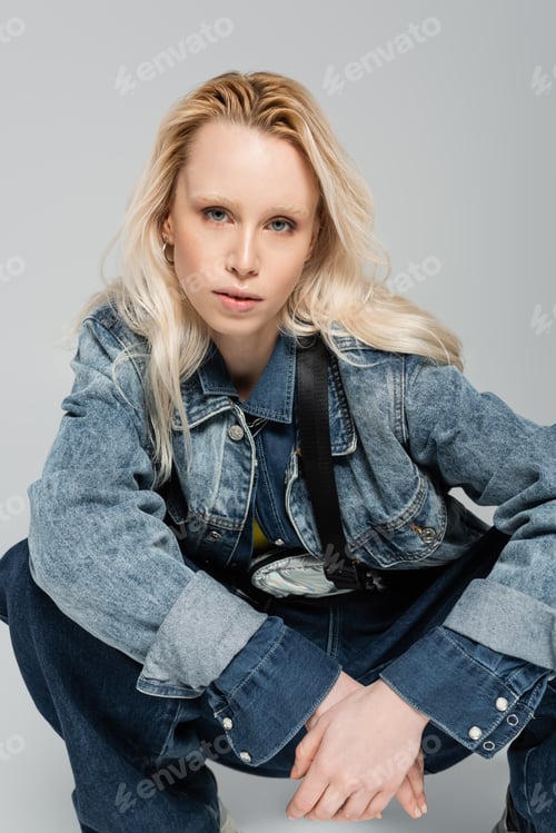 Preview: blonde albino woman in stylish denim jacket with belt bag posing isolated on grey
