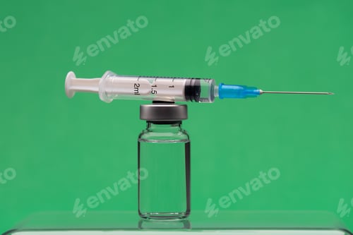 Preview: Syringe on top on a vaccine bottle, green background.