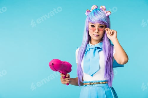 Preview: Asian anime girl in wig and glasses holding water gun isolated on blue
