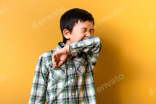 Preview: cute ill asian boy sneezing on yellow during self isolation