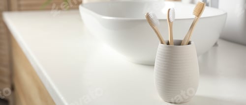 Preview: Bamboo toothbrushes in holder on white countertop in bathroom, space for text. Banner design