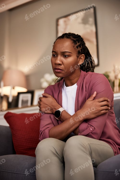 Preview: A pensive African-American woman sitting on the couch. looking sad.