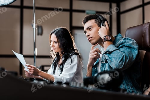 Preview: selective focus of concentrated mixed race sound producer in earphones near pretty colleague working