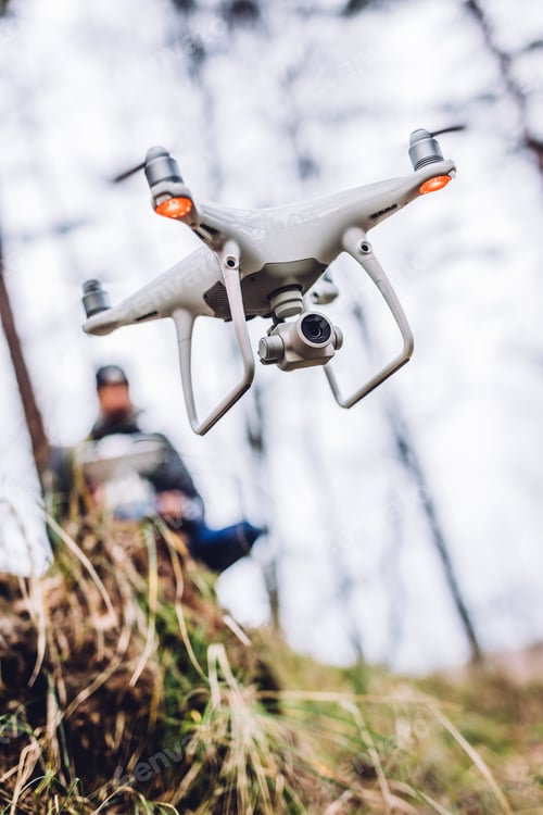Preview: Man with controller on hill in forest near flying drone