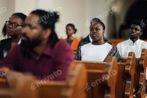 Preview: Young woman sitting in church pew with congregation listening to sermon