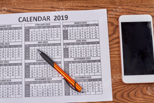 Preview: Year calendar with smartphone and pen on wooden desk.