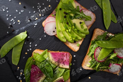Preview: top view of fresh toasts with vegetables on stone board with pepper and salt