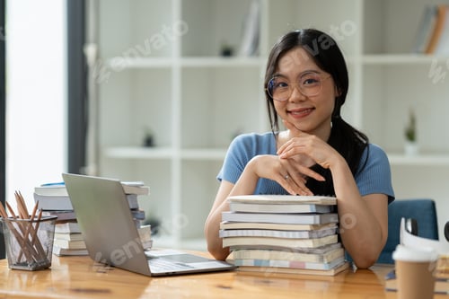 Preview: Asian woman in eyeglasses sitting on pile of books and laptop researching and relaxing. smile and be