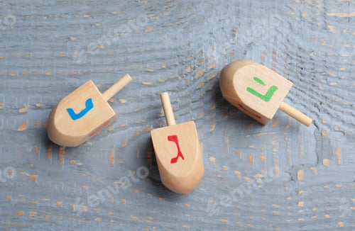 Preview: Hanukkah traditional dreidels with letters Nun, He and Gimel on grey wooden table, flat lay