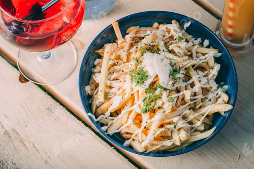 Preview: Bowl of french fries topped with sauce and refreshing drinks on a wooden table