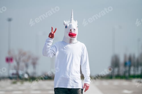 Preview: Man wearing unicorn mask making victory gesture with fingers