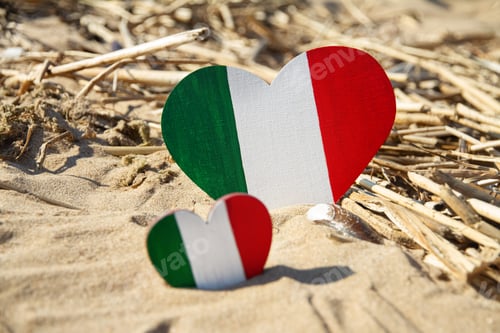 Preview: two wooden hearts painted in colors of flag Italy green white red lies on sand of beach