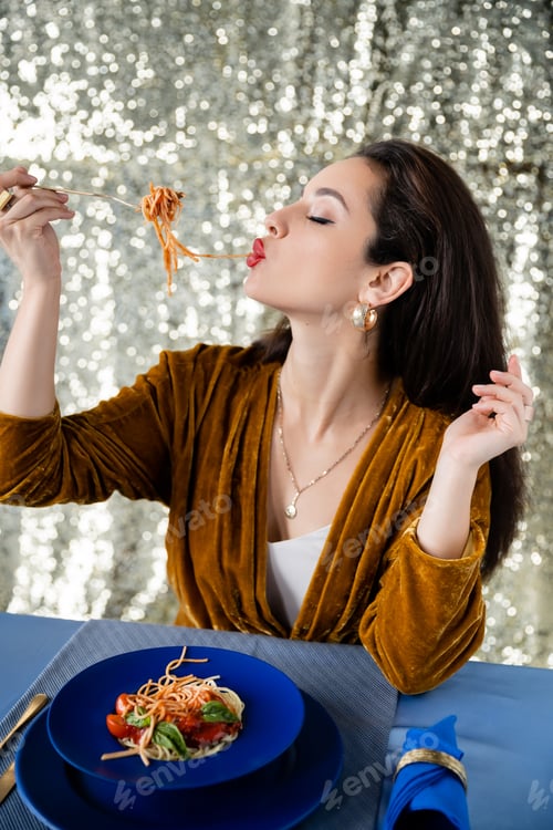 Preview: brunette woman eating tasty spaghetti near blue plates on shiny silver background