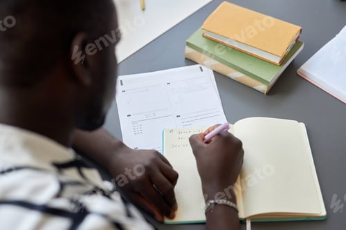 Preview: Close-up of young black man writing down formula or equation in copybook